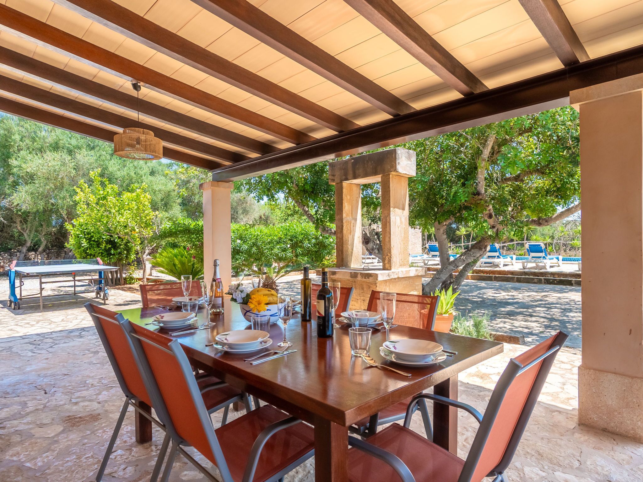 Un espacio para comer al aire libre con una mesa de madera dispuesta para seis personas, rodeada de sillas.