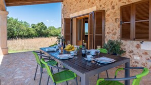 An outdoor dining area with a stone floor, wooden table, and green chairs. - Jardines by Interhome (Felanitx)