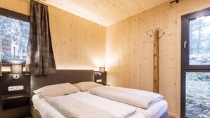 A wooden cabin bedroom with a bed, bedside lamps, and a window with curtains.