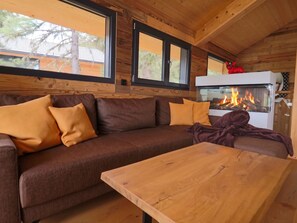 Een gezellige kamer met houten inrichting, een bank met kussens, een houten tafel en een open haard met vlammen.