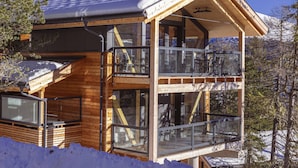 A wooden cabin with a balcony, large windows, and a snowy landscape. - 02_NTH004_Sup Chalet mit Sauna und Hot Tub 2 Etage by Interhome (Turracher Höhe)