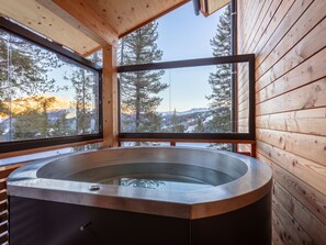 Een hottub in een houten chalet met grote ramen en uitzicht op de bergen.