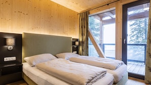 A wooden cabin bedroom with two beds, a nightstand, a lamp, and a window with curtains. - 02_NTH004_Sup Chalet mit Sauna und Hot Tub 2 Etage by Interhome (Turracher Höhe)