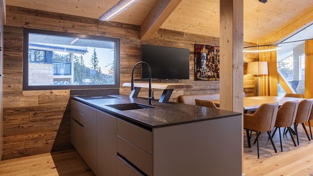 A modern kitchen with a large island, a built-in TV, and a dining area with wooden furniture. - 02_NTH004_Sup Chalet mit Sauna und Hot Tub 2 Etage by Interhome (Turracher Höhe)