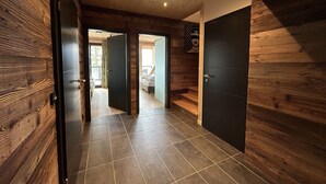 A hallway with wooden walls and a tiled floor, leading to a bedroom with a bed and a window.
