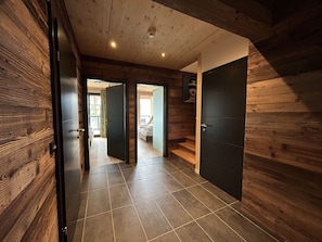 A hallway with wooden walls and a tiled floor, leading to a bedroom with a bed and a window. - 02_NTH004_Sup Chalet mit Sauna und Hot Tub 2 Etage by Interhome (Turracher Höhe)