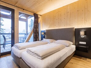 A modern hotel room with a large bed, a small bedside table, and a view of the outdoors through a glass door. - 02_NTH004_Sup Chalet mit Sauna und Hot Tub 2 Etage by Interhome (Turracher Höhe)