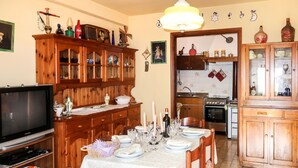 Een eetkamer met een houten tafel gedekt voor vier personen, een televisie op een standaard en een keuken op de achtergrond.
