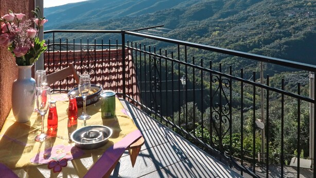 Een balkon met een eettafel, met uitzicht op een bergachtig landschap.