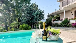 Mesa junto a la piscina con una botella de champán, una copa y una cesta de flores.