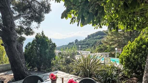 Un área de comedor al aire libre con una mesa dispuesta para dos personas, rodeada de follaje y con vistas a un paisaje pintoresco.