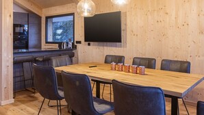 Eine moderne Küche mit großem Fenster, einem Essbereich mit Holztisch und -stühlen sowie einem an der Wand befestigten Flachbildfernseher.