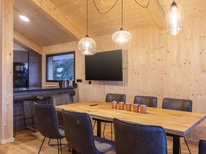 Eine moderne Küche mit großem Fenster, einem Essbereich mit Holztisch und -stühlen sowie einem an der Wand befestigten Flachbildfernseher.