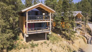 Eine zweistöckige Holzhütte mit Balkon, umgeben von dichtem Wald.