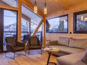 A cozy interior with a wooden ceiling, large windows, a sofa, two armchairs, and a small round table.