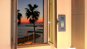 Una stanza con un'ampia finestra che si affaccia su una spiaggia al tramonto, una lampada e una porta.