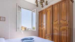 Une chambre à coucher avec une grande armoire en bois, un lit recouvert d’une courtepointe blanche et une fenêtre donnant sur un bâtiment à l’extérieur.