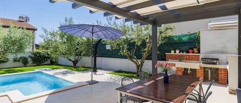 A covered patio with a pool, outdoor seating, and a barbecue area.