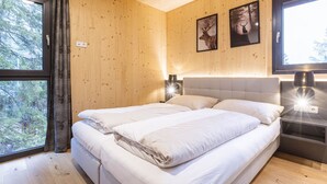 A wooden-paneled bedroom with a bed, two bedside tables with lamps, and two framed pictures on the wall. - 02_NTH005_Sup Chalet mit Sauna und Hot Tub 2 Etage by Interhome (Turracher Höhe)