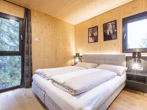 Een slaapkamer met houten lambrisering, een bed, twee nachtkastjes met lampen en twee ingelijste foto's aan de muur.