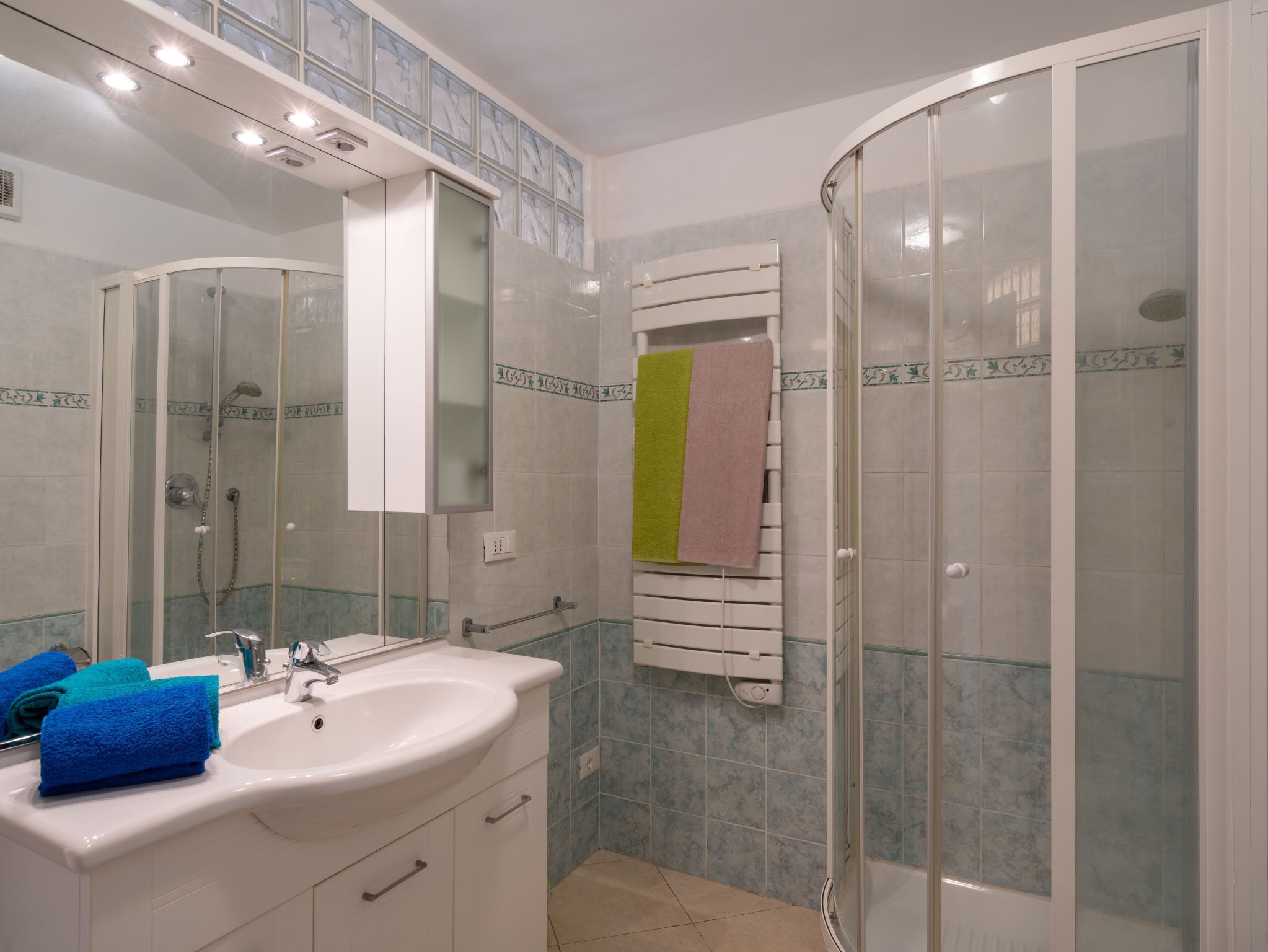 Ein Badezimmer mit Waschbecken, Spiegel, Duschkabine und Handtuchhalter.