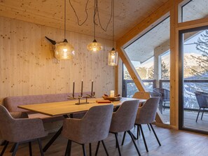 Un espace repas avec une table en bois, des bancs rembourrés et des luminaires suspendus.
