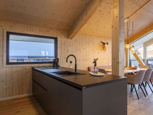 Una cocina moderna con un ventanal grande, vigas de madera en el techo y un comedor con sillas.