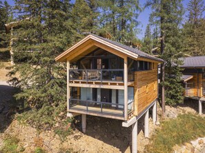 Eine zweistöckige Holzhütte mit einem Balkon im oberen Stockwerk, umgeben von Bäumen.
