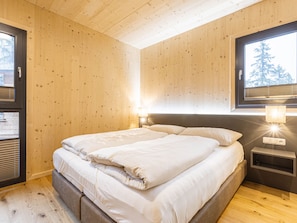 Een kamer met houten lambrisering, een bed, bedlampen en een raam met zonwering.