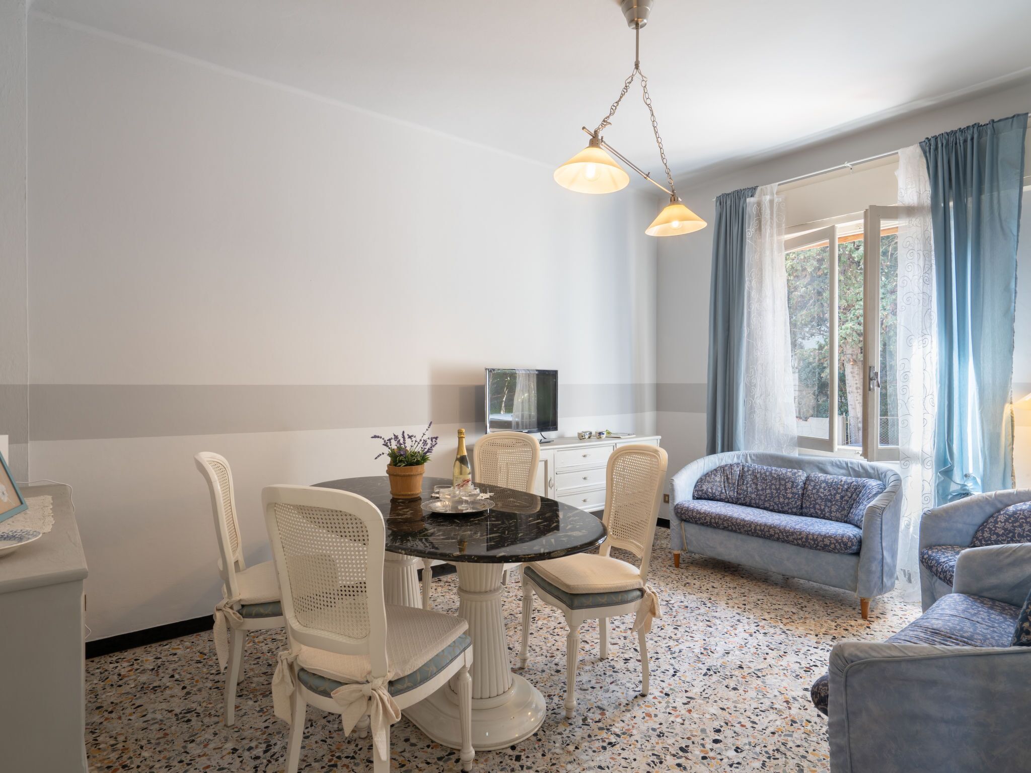 A dining area with a round table, white chairs, a television, and a sofa.