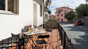 A terrace with outdoor seating, a table with chairs, and a view of the street and neighboring buildings. - Cipressi by Interhome (San Lorenzo al Mare)