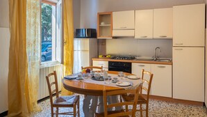 A compact kitchen with a dining table, chairs, a refrigerator, a microwave, a stove, and a sink. - Cipressi by Interhome (San Lorenzo al Mare)