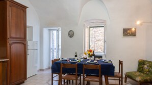 A dining area with a table set for four, a wooden cabinet, and a window with a view of a stone wall. - Le Antiche Volte (SLR215) by Interhome (San Lorenzo al Mare)