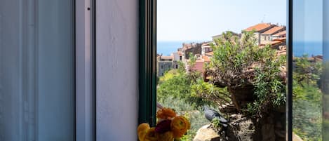 A window with a view of a coastal town, a rock with plants, and a vase of flowers.