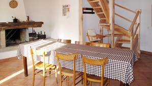 Ein rustikaler Essbereich mit Holztisch und -stühlen, einem Kamin und einer Holztreppe.