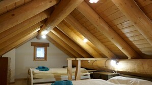 Ein gemütliches Schlafzimmer im Dachgeschoss mit Holzbalken, zwei Betten und einem kleinen Fenster.