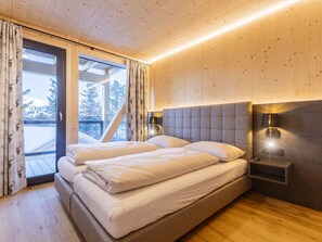 A bedroom with a bed, two bedside lamps, a window with curtains, and a view of trees outside.