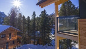 A wooden cabin with a glass balcony overlooking a snowy landscape and a clear sky.