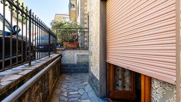 Une ruelle étroite avec un pavé de pierre, une clôture en métal, un pot de fleurs et un bâtiment dont le volet est fermé.