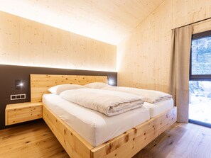Un dormitorio de madera con una cama, mesitas de noche y una ventana con vistas a árboles.