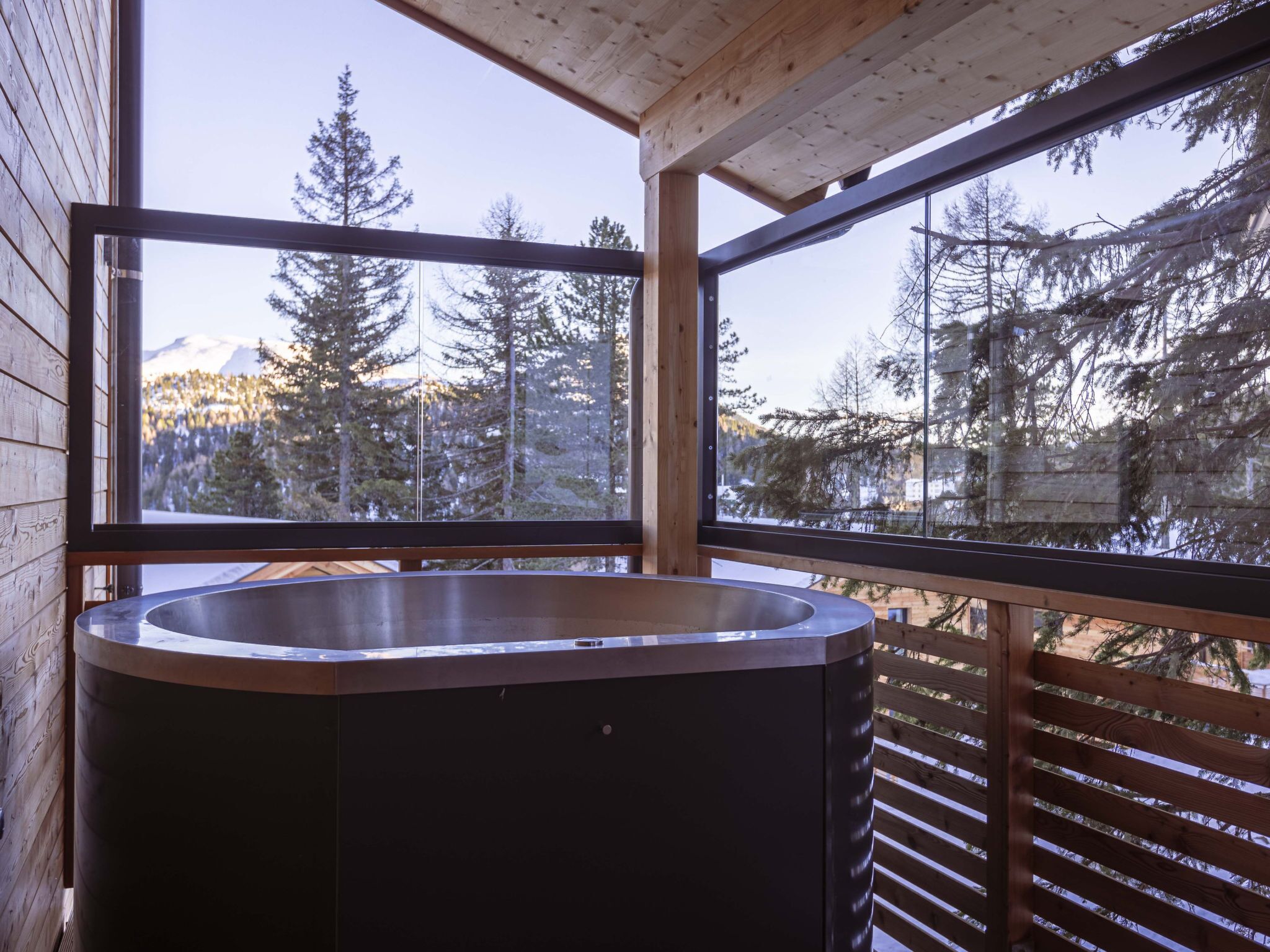 Eine Holzhütte mit Whirlpool auf einem Balkon, mit Blick auf eine bewaldete Berglandschaft.