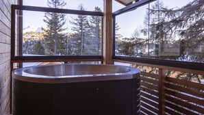 Une cabane en bois dotée d’un jacuzzi sur un balcon, offrant une vue sur une région montagneuse boisée.