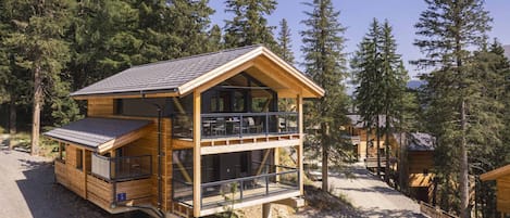 A two-story wooden cabin with a balcony, surrounded by trees.