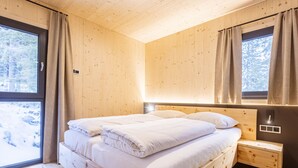 Une chambre dans une cabane en bois, avec un lit, une table de chevet et une fenêtre avec des rideaux.