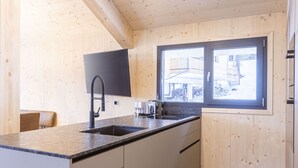 Une cuisine avec des murs en bois, une fenêtre, un évier, un grille-pain et une chaise.