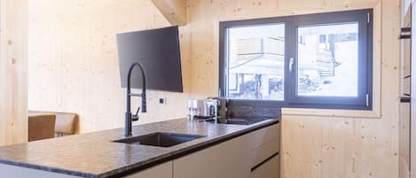 A kitchen with wooden walls, a window, a sink, a toaster, and a chair.