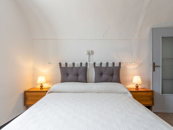 A bedroom with a bed, two bedside tables with lamps, a headboard with curtains, and a door.