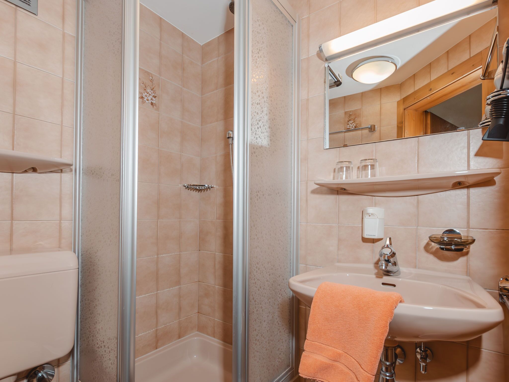 Un baño con ducha envuelta en vidrio, un lavabo con toalla y un espejo sobre él.