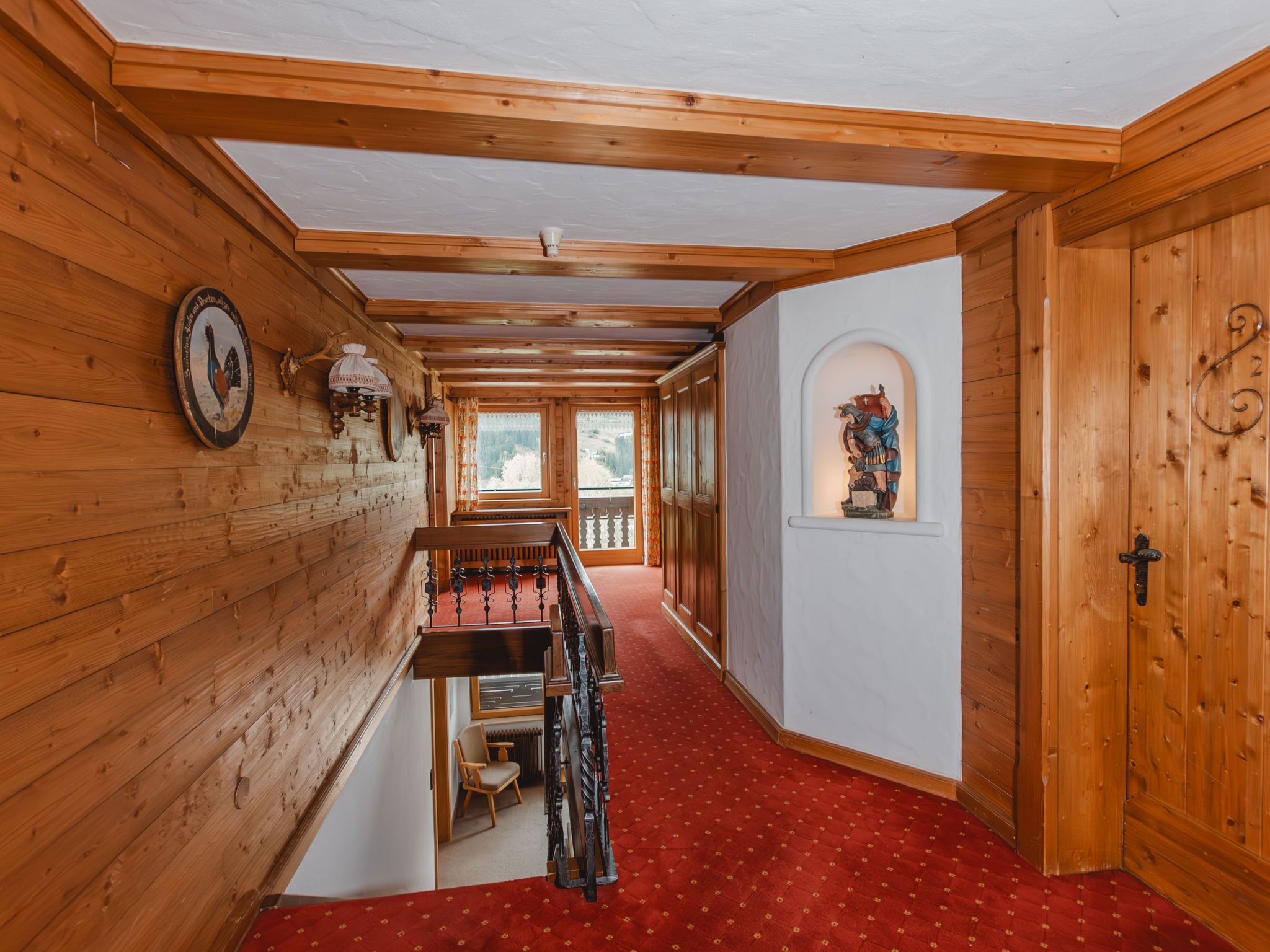 Un interior de madera con alfombra roja, vigas de madera, una escalera y una vista a través de una ventana.