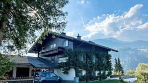 Ein zweigeschossiges Haus mit Balkon, ein Auto auf der Einfahrt und ein Holzzaun.